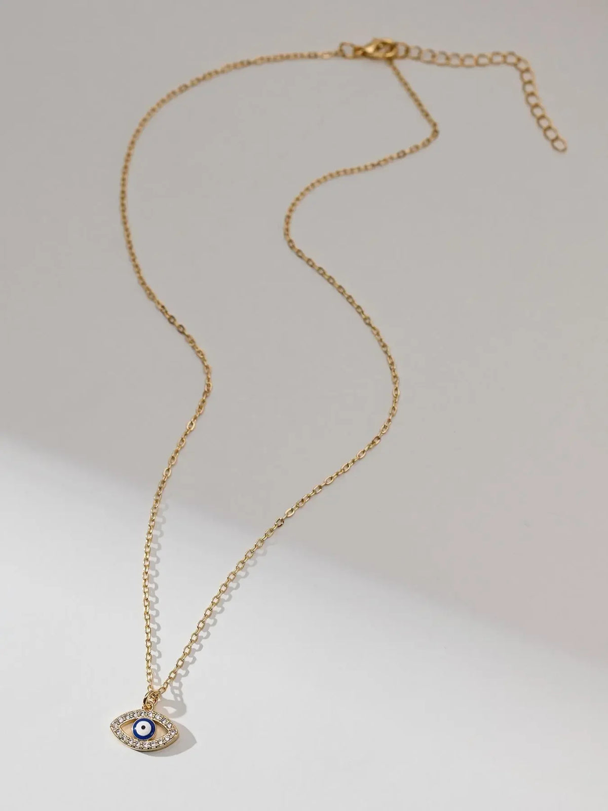 Full gold-tone evil eye necklace with extender chain laid on a light background