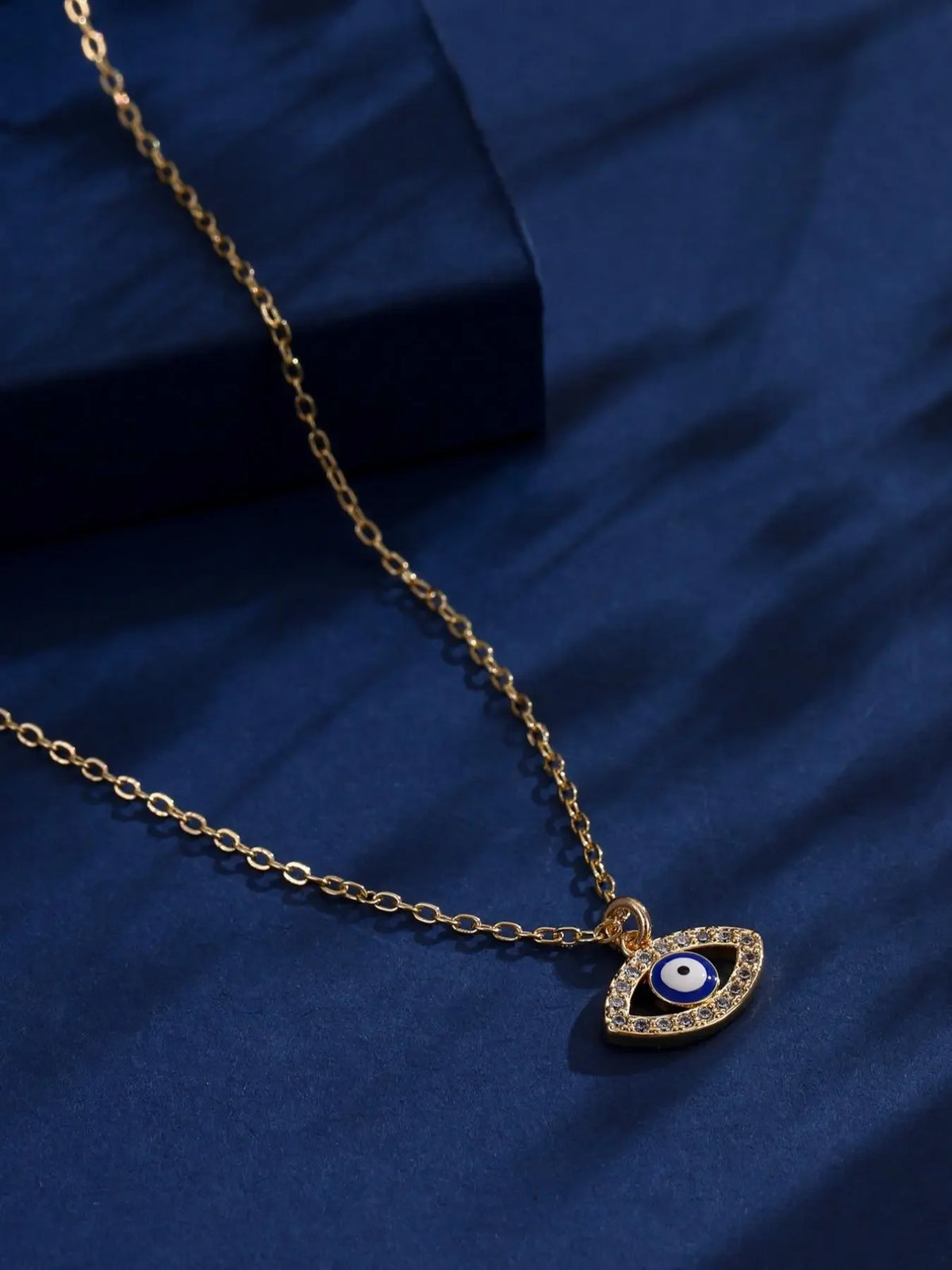 Gold-tone evil eye pendant necklace displayed on navy fabric