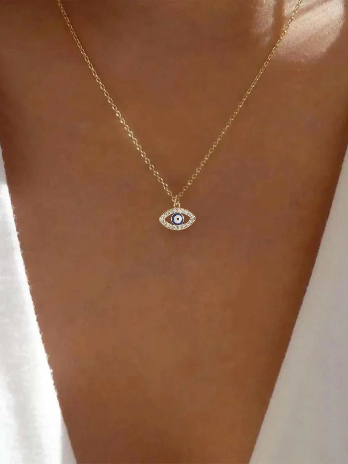 Gold-tone evil eye pendant necklace with a blue-and-white center worn at the neckline