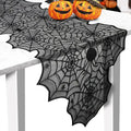 Black spiderweb lace runner draped over a white table with pumpkin decorations