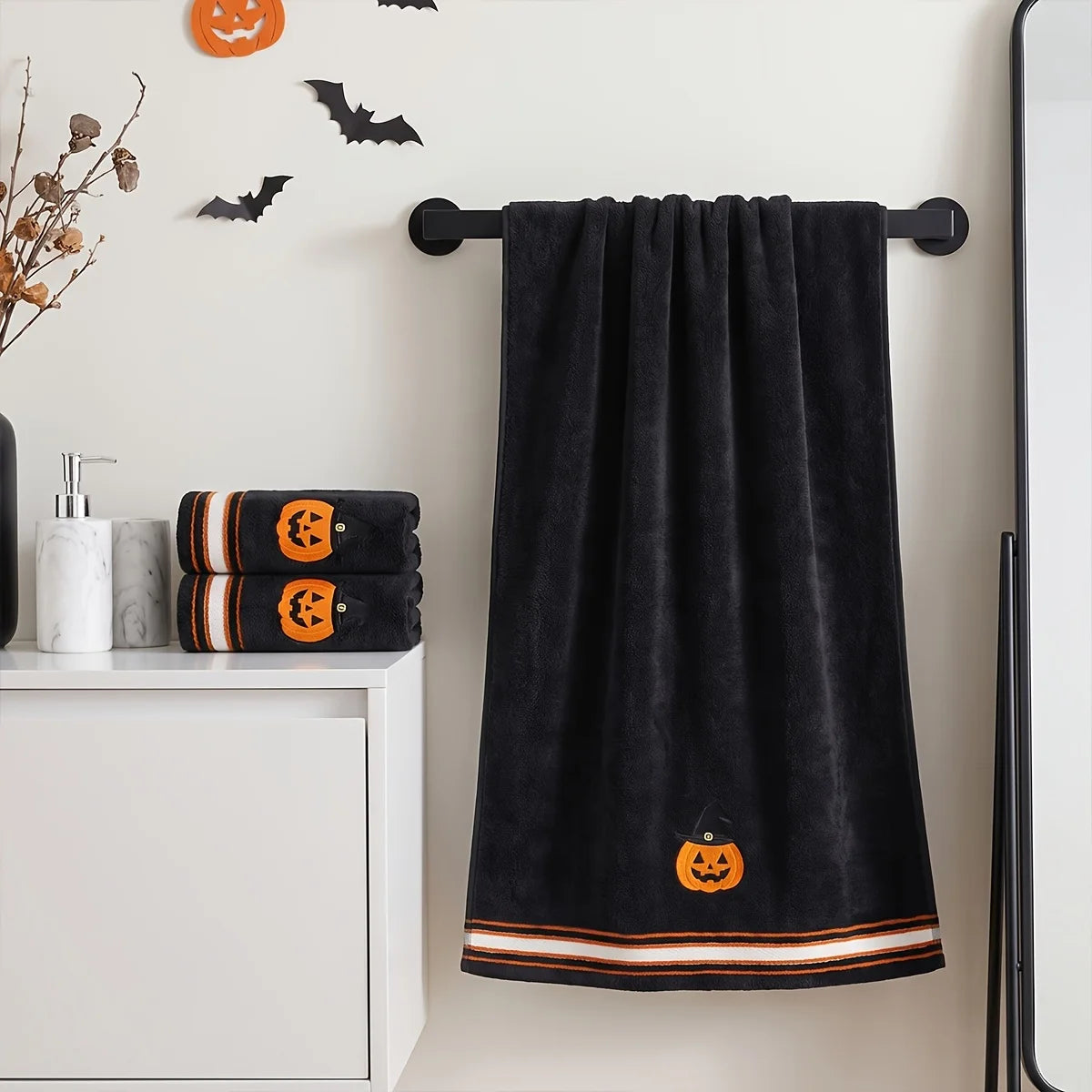 Black pumpkin bath towel hanging on a bathroom rail with matching folded hand towels